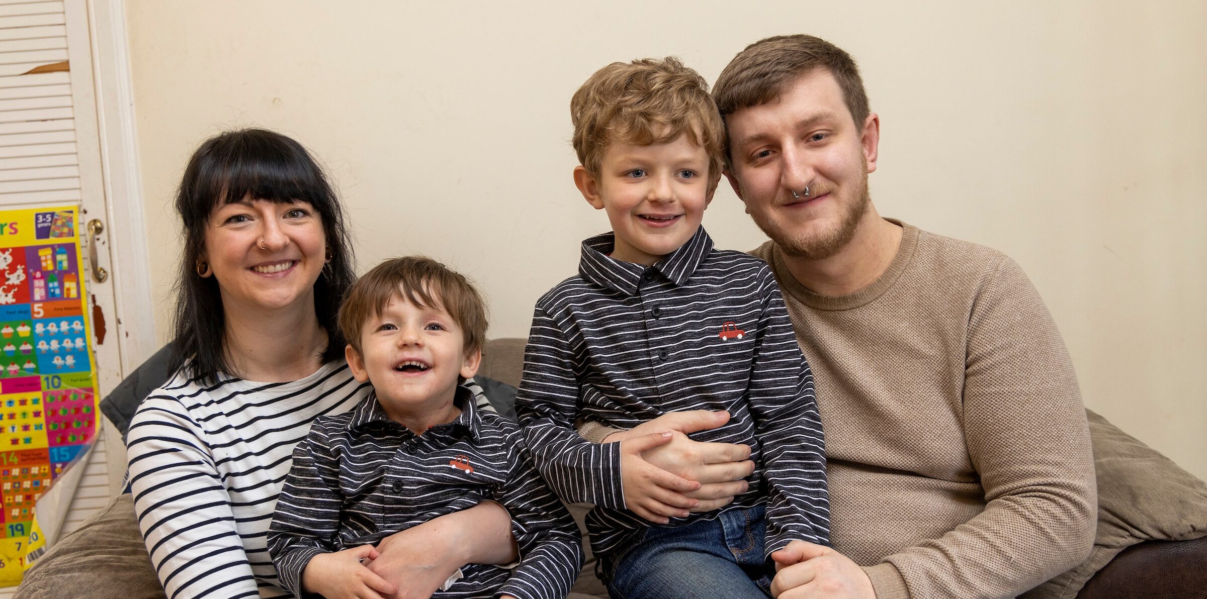A supported family sit on the sofa. Mum, Dad and two young boys.