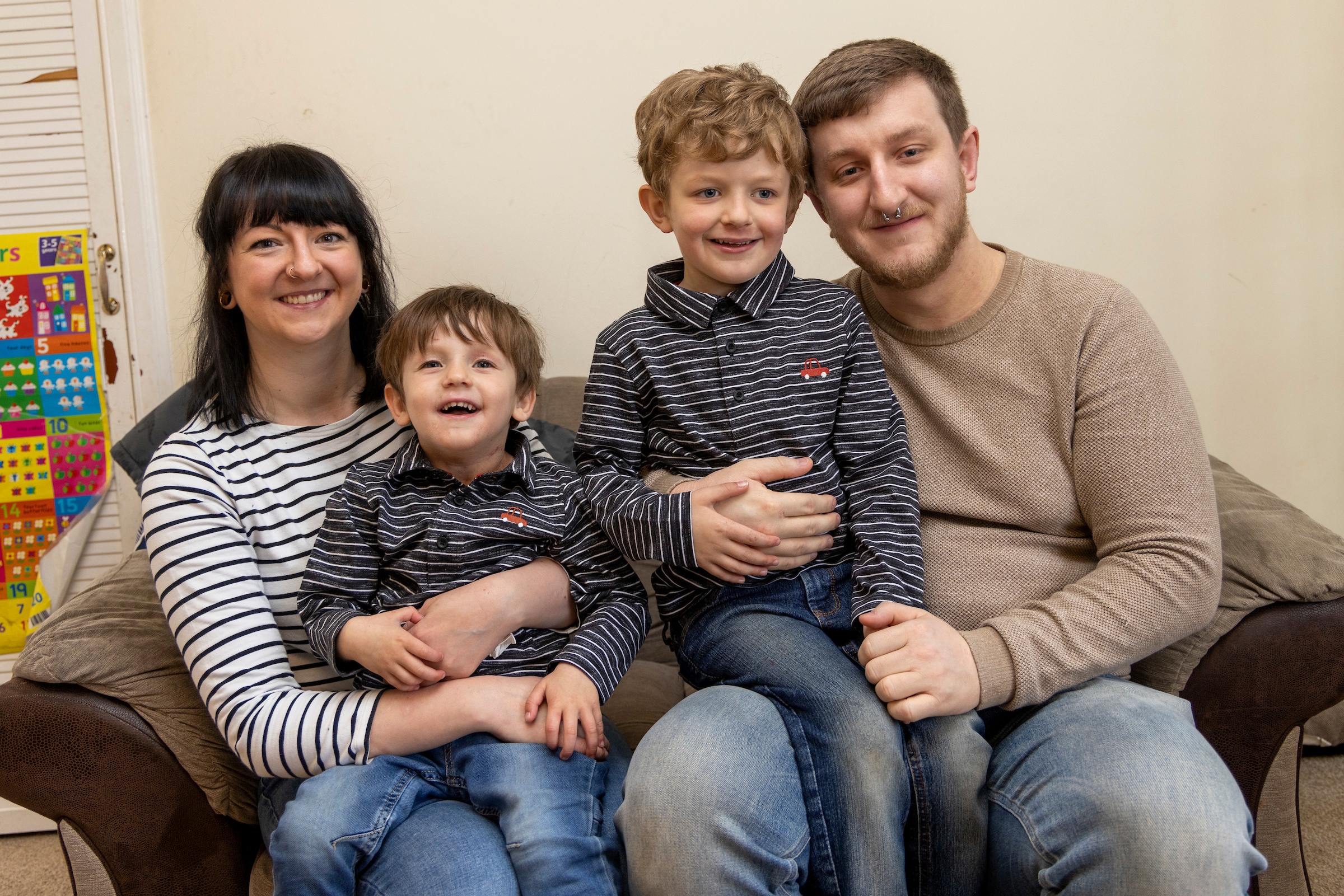 A supported family sit on the sofa. Mum, Dad and two young boys.